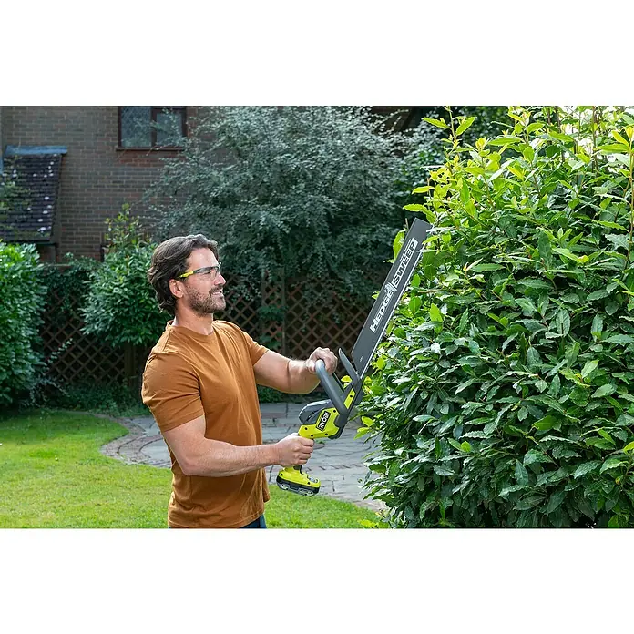 Ryobi ONE+ Akku-Heckenschere RY18HT45A-0 - 18 V, Li-Ionen, Ohne Akku - Mann trimmt Hecke mit Ryobi Hedge Sweep Heckenschere, Schutzbrille tragend, im Garten.