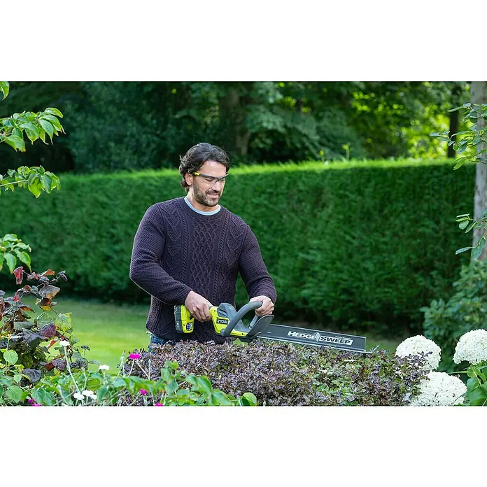 Ryobi ONE+ Akku-Heckenschere RY18HT45A-0 - 18 V, Li-Ionen, Ohne Akku - Ein Mann benutzt eine Ryobi Heckenschere, um Büsche in einem Garten zu schneiden, wobei der Fokus auf dem Werkzeug liegt.