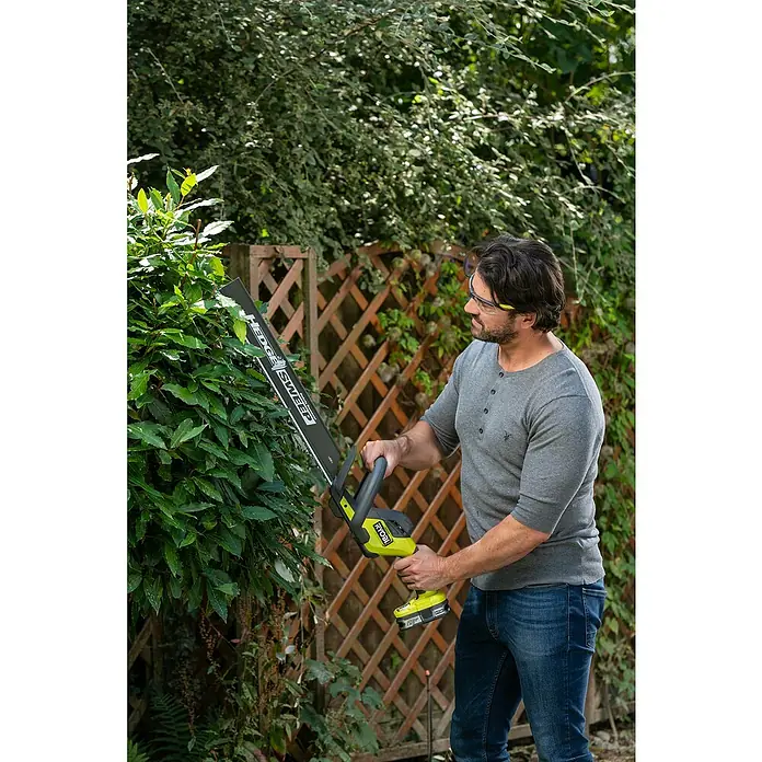 Ryobi ONE+ Akku-Heckenschere RY18HT50A-0 - 18 V, Li-Ionen, Ohne Akku - Ein Mann schneidet eine Hecke mit einer RYOBI Akku-Heckenschere. Das Gerät ist gelb und schwarz und hat eine lange Schneide.