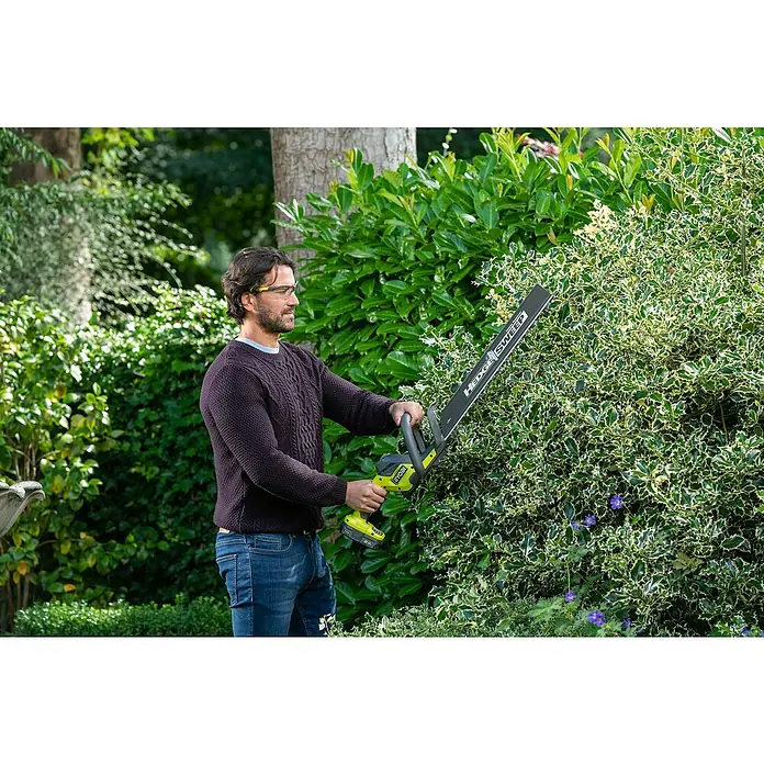 Ryobi ONE+ Cortasetos de batería RY18HT50A-0 - 18 V, Iones de litio, Sin batería - Un hombre usa un cortasetos Ryobi para recortar un seto. El cortasetos Ryobi es inalámbrico y tiene una hoja larga.