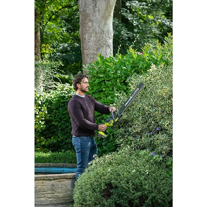 Ryobi ONE+ Akku-Heckenschere RY18HT50A-125 - 18 V, Li-Ionen, 1 Akku - Ein Mann benutzt eine Ryobi Heckenschere, um eine Hecke zu schneiden. Das Gerät ist mit einem grünen Griff und einem schwarzen Schneidblatt ausgestattet.
