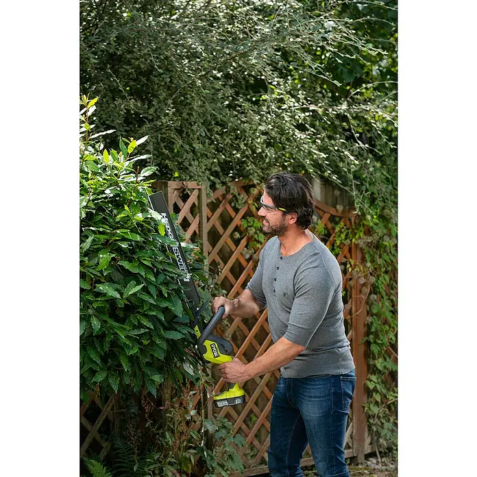 Ryobi ONE+ Akku-Heckenschere RY18HT50A-0 - 18 V, Li-Ionen, Ohne Akku - Mann trimmt Hecke mit Ryobi Akku-Heckenschere, trägt Schutzbrille. Ideale Gartengeräte für präzise Formschnitte und mühelose Gartenpflege.