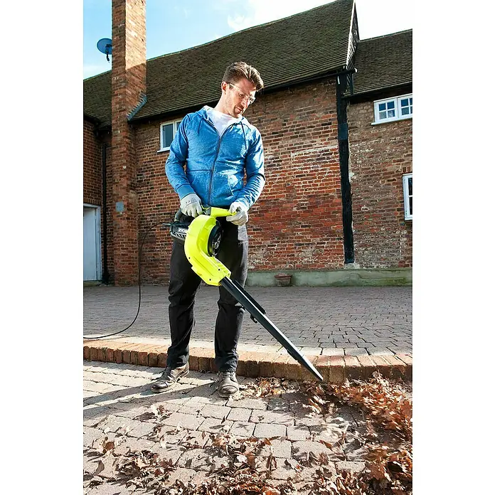 Ryobi Elektro-Laubsauger RBV3000CESV - 3.000 W, Blasgeschwindigkeit: 375 km/h, Blasleistung: 14 m³/min - Ein Mann benutzt einen Laubbläser, um Blätter von einer gepflasterten Fläche zu entfernen. Er trägt Schutzbrille und Handschuhe.