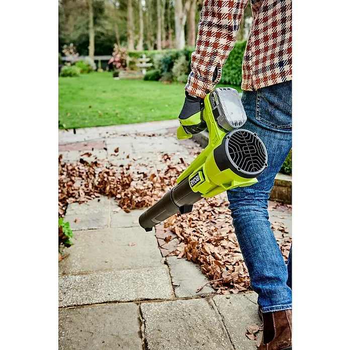 Ryobi ONE+ Soplador de hojas de batería RY18BLA - 18 V, Sin batería, Velocidad de soplado: 145 km/h, Potencia de soplado: 7,1 m³/min - Una persona usa un soplador de hojas amarillo de la marca Ryobi para quitar hojas de un camino pavimentado.