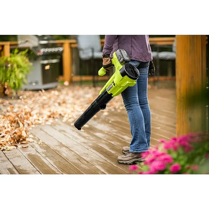 Ryobi ONE+ Akku-Laubbläser RY18BLA-0 - 18 V, Ohne Akku, Blasgeschwindigkeit: 145 km/h, Blasleistung: 7,1 m³/min - Die Person hält einen RYOBI Akku-Laubbläser auf einer nassen Holzterrasse mit herabgefallenen Blättern.