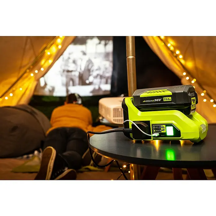 Ryobi Max Power Wechselrichter RY36BI300A-0 - 36 V, Ohne Akku, 300 W - Ein grüner Ryobi-Stromgenerator mit Akku steht auf einem Tisch und versorgt einen Projektor in einem Zelt mit Strom.