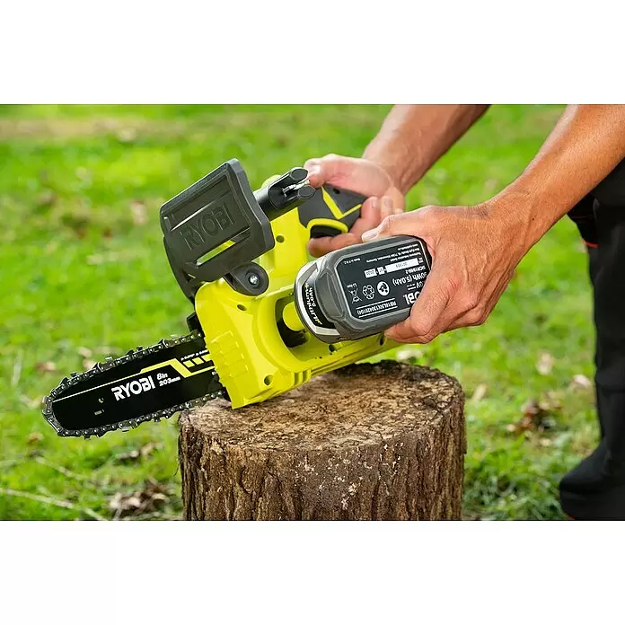 Ryobi ONE+ Akku-Kettensäge RY18CS20A-0 - 18 V, Li-Ionen, Ohne Akku, Schwertlänge: 20 cm - Person setzt Akku in gelbe Ryobi Akku-Kettensäge mit schwarzer Kette auf einem Baumstumpf ein.