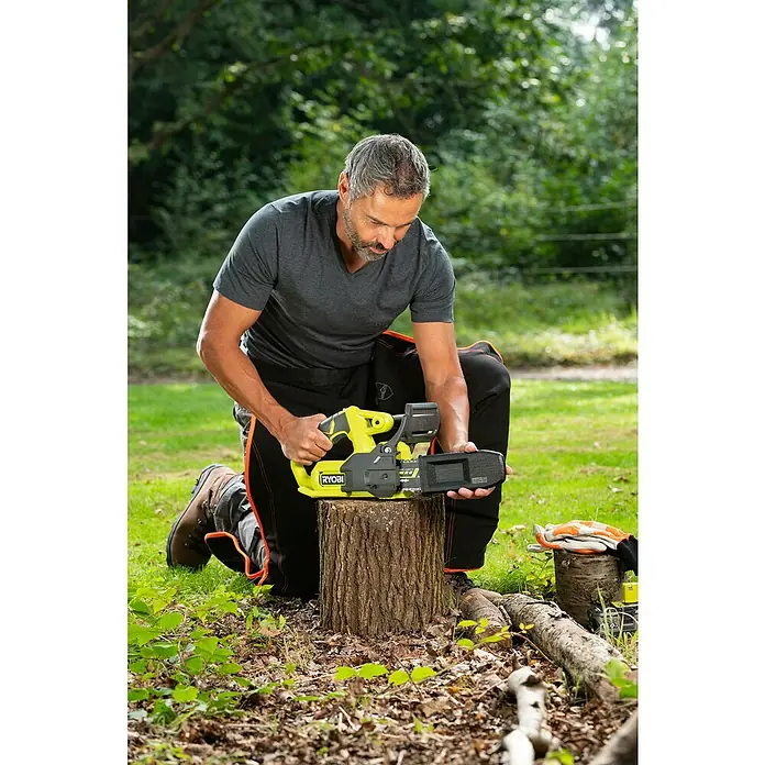 Ryobi ONE+ Akku-Kettensäge RY18CS20A-0 - 18 V, Li-Ionen, Ohne Akku, Schwertlänge: 20 cm - Ein Mann kniet im Freien und benutzt eine gelbe RYOBI-Kettensäge auf einem Baumstumpf. Die Kettensäge steht im Fokus.