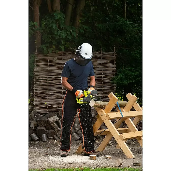 Ryobi ONE+ Akku-Kettensäge RY18CS20A-0 - 18 V, Li-Ionen, Ohne Akku, Schwertlänge: 20 cm - Person schneidet sicher einen Holzstamm mit einer limettengrünen Ryobi Kettensäge auf einem Sägebock, trägt Schutzhelm, Visier und Schutzkleidung.