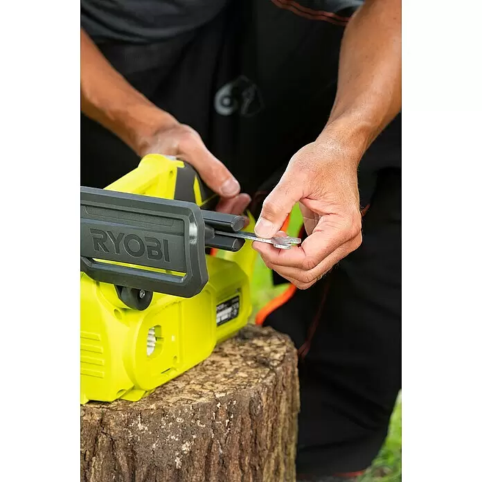 Ryobi ONE+ Akku-Kettensäge RY18CS20A-0 - 18 V, Li-Ionen, Ohne Akku, Schwertlänge: 20 cm - Eine Person justiert eine leuchtend grüne und schwarze RYOBI Kettensäge mit einem Metallschlüssel auf einem Holzstumpf.