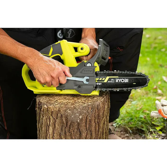 Ryobi ONE+ Akku-Kettensäge RY18CS20A-0 - 18 V, Li-Ionen, Ohne Akku, Schwertlänge: 20 cm - Ein Mann spannt die Kette einer gelben Ryobi Akku-Kettensäge mit einem Schraubenschlüssel, die auf einem Baumstumpf steht.