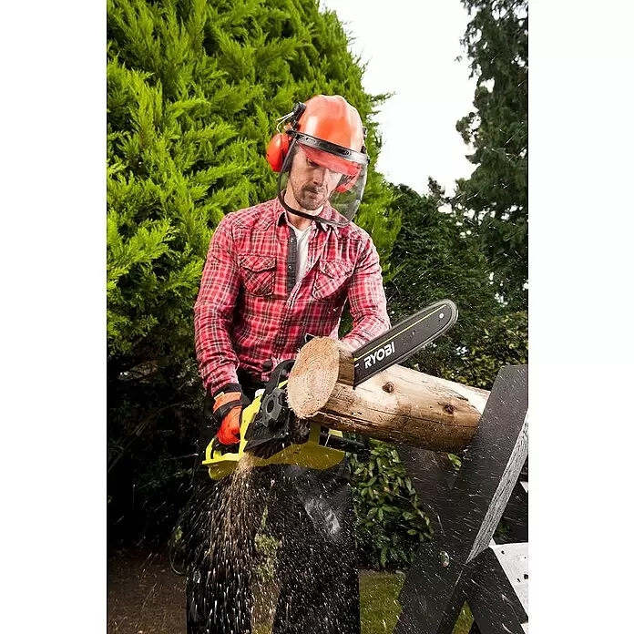 Ryobi Elektro-Kettensäge RCS2340B - 2.300 W, Schwertlänge: 40 cm - Mann in Schutzausrüstung schneidet einen Stamm mit einer gelb-schwarzen RYOBI Kettensäge, Späne fliegen.