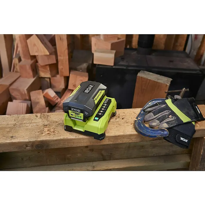 Ryobi Schnellladegerät RY36C60A - Passend für: Alle Ryobi Power Max Akkus, 6 A, 36 V - Nahaufnahme eines RYOBI Akku-Ladegeräts mit eingesetztem Akku, platziert auf einer Werkbank neben Arbeitshandschuhen und einer Zwinge.
