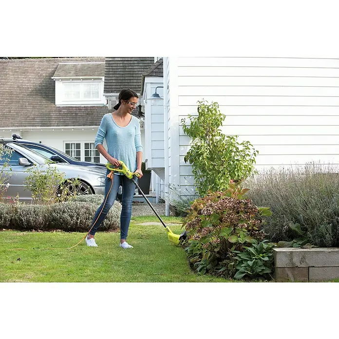 Ryobi Elektro-Rasentrimmer RLT3525 - 350 W, Schnittbreite Faden: 25 cm - Eine Frau, die einen Rasentrimmer benutzt, um den Rasen um einen Garten zu pflegen.