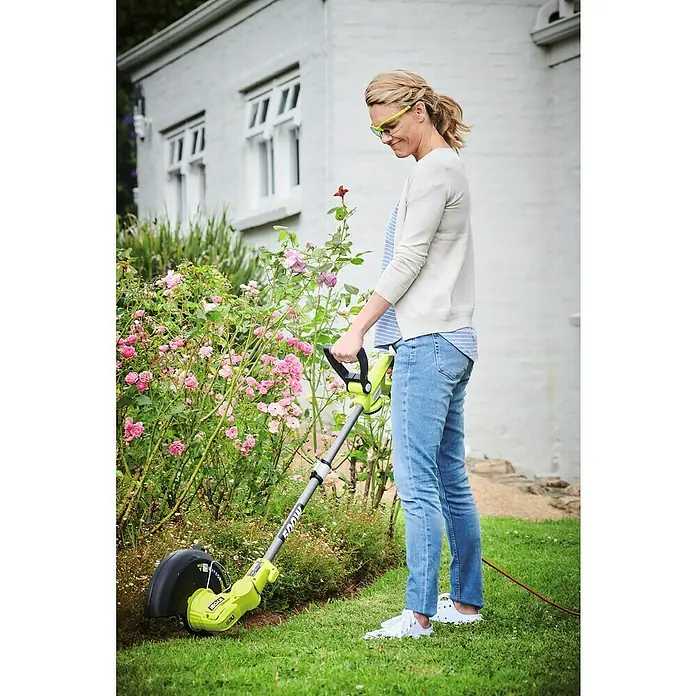 Ryobi Elektro-Rasentrimmer RLT5127 - 500 W, Schnittbreite Faden: 27 cm - Frau trimmt den Rasen mit dem Ryobi Rasentrimmer, um einen gepflegten Garten zu erhalten, geschützt durch gelbe Schutzbrillen.