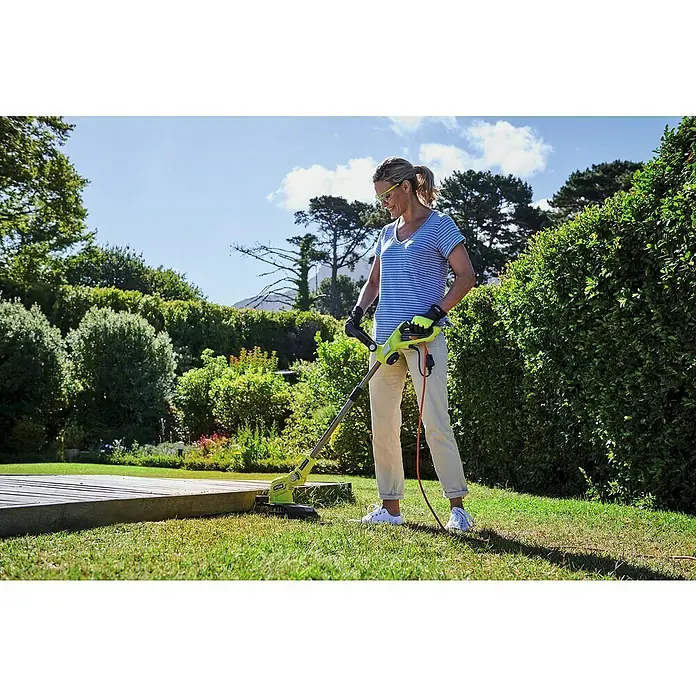 Ryobi Elektro-Rasentrimmer RLT5127 - 500 W, Schnittbreite Faden: 27 cm - Frau benutzt Ryobi Trimmer zum Trimmen von Gras in einem Garten mit grünen Büschen und Bäumen an einem sonnigen Tag.