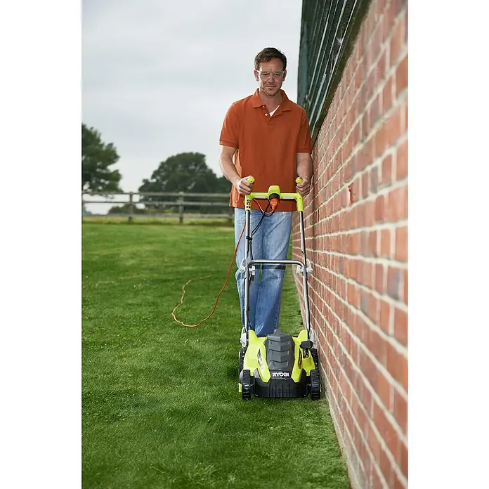 Ryobi Elektro-Rasenmäher RLM15E36H - 1.500 W, Schnittbreite: 36 cm - Ein Mann mäht den Rasen mit einem gelb-schwarzen RYOBI Rasenmäher entlang einer Ziegelmauer.
