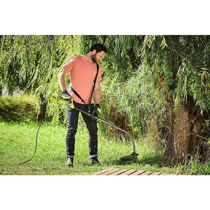 Ryobi Elektro-Motorsense RBC1226I - 1.200 W, Schnittbreite Faden: 38 cm, Schnittbreite Messer: 26 cm - Ein Mann trimmt Gras mit einem RYOBI Rasentrimmer in seinem Garten, umgeben von üppigem Grün.