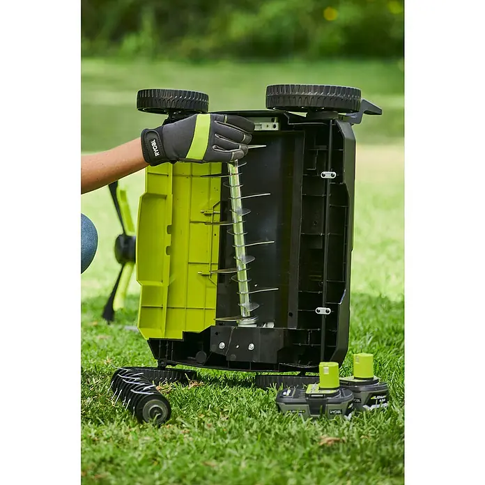 Ryobi ONE+ Escarificador de batería RY18SFX35A-0 - Número de baterías: Sin batería, 18 V, Anchura de trabajo: 35 cm - Un aireador de césped Ryobi es sostenido por una mano enguantada, mostrando las púas. Baterías al lado.