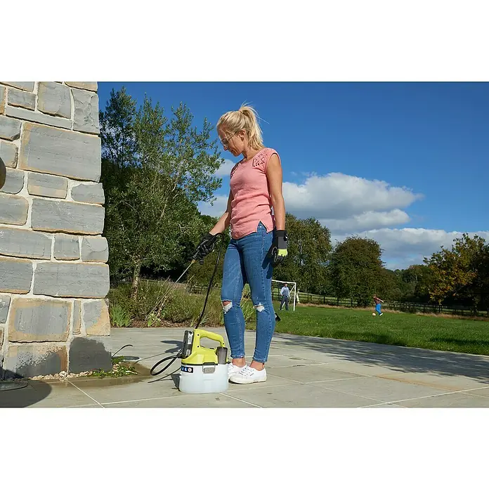 Ryobi ONE+ Akku-Sprühgerät OWS1880 - 18 V, Anzahl Akkus: Ohne Akku, 3,5 l - Frau verwendet einen Ryobi-Sprühapparat, um Unkraut zu entfernen, während im Hintergrund Kinder Fußball spielen.