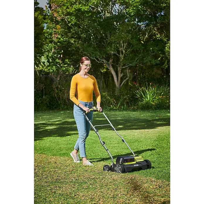 Ryobi ONE+ Escarificador de batería RY18SFX35A-0 - Número de baterías: Sin batería, 18 V, Anchura de trabajo: 35 cm - Una mujer usa una cortadora de carrete RYOBI en su jardín vestida con ropa amarilla y jeans para mantener el césped.