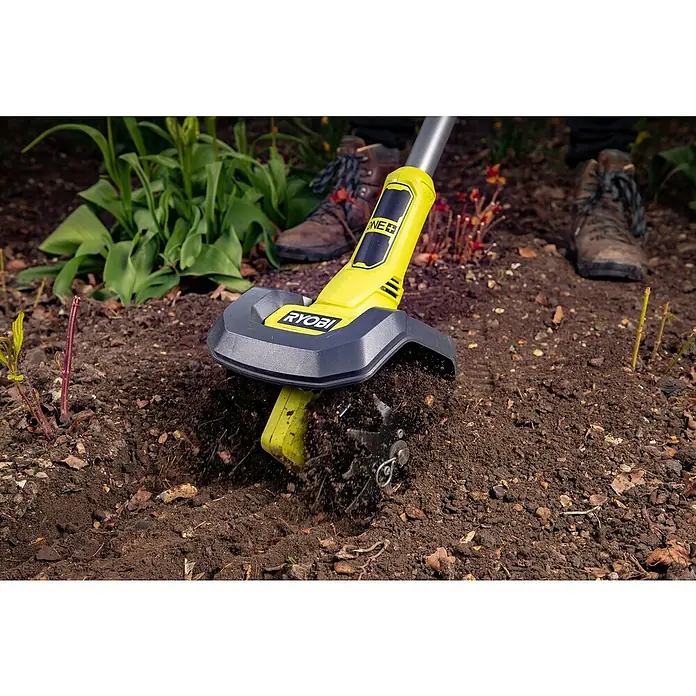 Ryobi ONE+ Akku-Bodenhacke RY18CVA-0 - Ohne Akku, Li-Ionen, 18 V - Der Ryobi-Bodenbearbeiter lockert den Boden in einem Garten auf, wobei braune Stiefel im Hintergrund zu sehen sind.