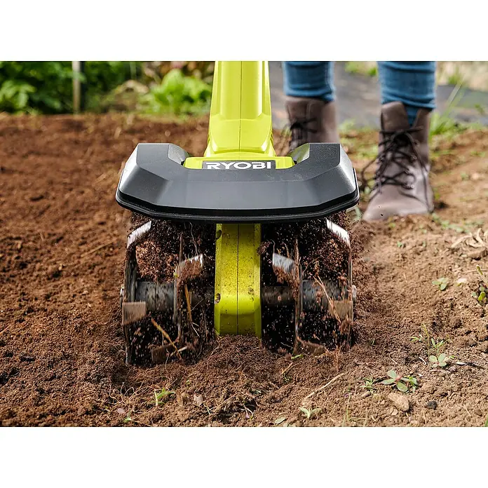Ryobi ONE+ Akku-Bodenhacke RY18CVA-0 - Ohne Akku, Li-Ionen, 18 V - Nahaufnahme eines Ryobi Kultivators, der Erde bearbeitet, mit Stiefeln im Hintergrund.