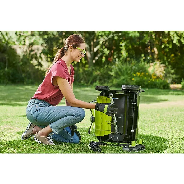 Ryobi ONE+ Escarificador de batería RY18SFX35A-0 - Número de baterías: Sin batería, 18 V, Anchura de trabajo: 35 cm - Una mujer se agacha en el jardín inspeccionando un aireador de césped verde y negro.