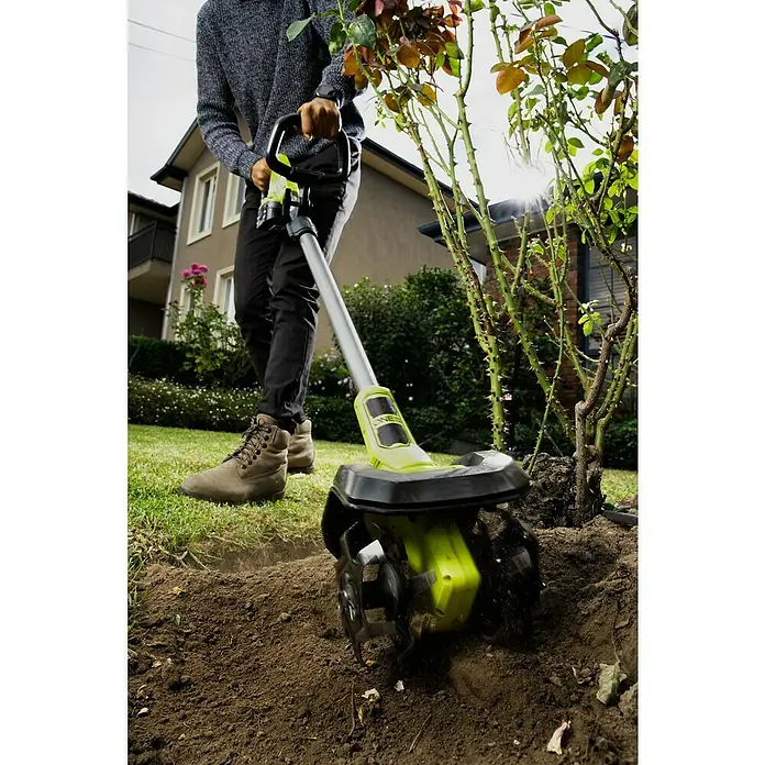 Ryobi ONE+ Akku-Bodenhacke RY18CVA-0 - Ohne Akku, Li-Ionen, 18 V - Nahaufnahme eines Mannes, der einen grünen und schwarzen Kultivator zum Auflockern der Erde in einem Garten benutzt.