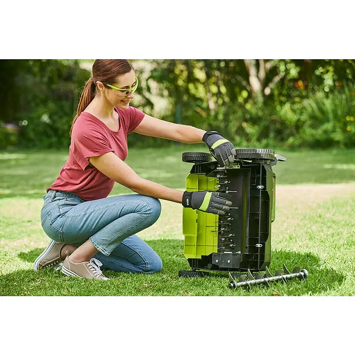 Ryobi ONE+ Akku-Vertikutierer RY18SFX35A-0 - Anzahl Akkus: Ohne Akku, 18 V, Arbeitsbreite: 35 cm - Eine Frau hockt im Garten und montiert eine Ryobi Rasenlüfter/Vertikutierer-Kombination, wobei sie Schutzbrille und Gartenhandschuhe trägt.