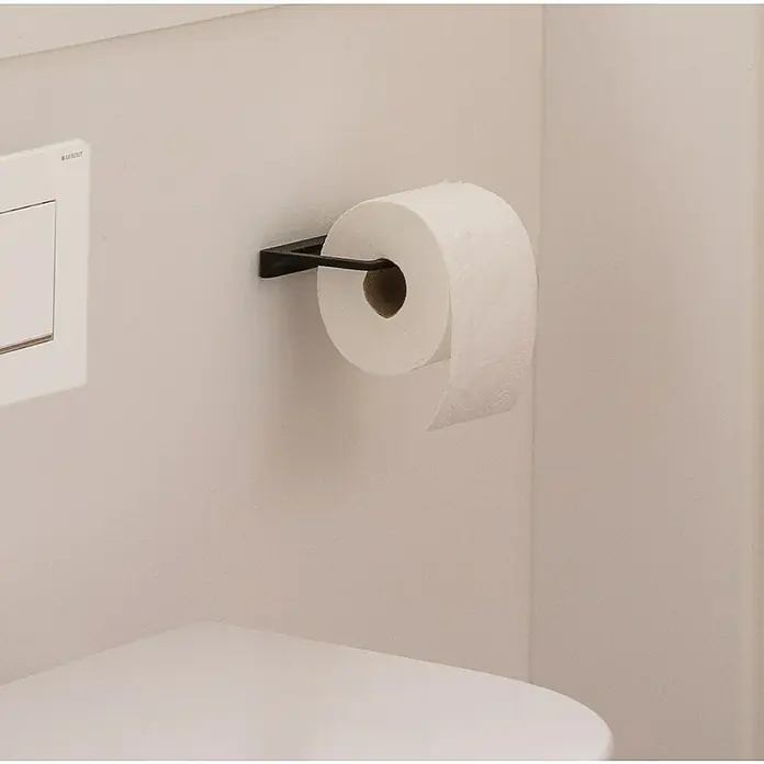 Phoenix Toilettenpapierhalter - Ohne Deckel, Schwarz, Matt - Toilettenpapier auf einem eleganten, schwarzen Halter, montiert an einer hellen Badezimmerwand, neben einem modernen Betätigungsfeld.