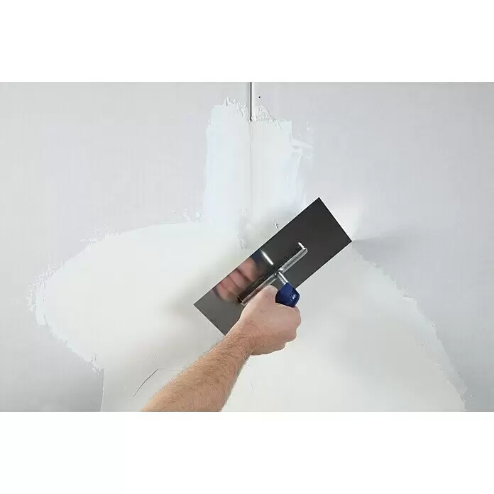 Rigips VARIO Fugenspachtel Finish - 5 kg - Hand hält eine Edelstahl-Gipsspachtel mit blauem Griff, die weißen Putz auf eine Wand aufträgt.