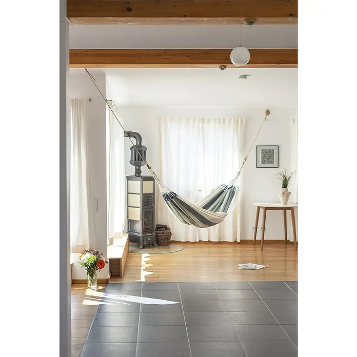 La Siesta Hängematte Modesta - L x B: 300 x 140 cm, Olive, Single - Innenaufnahme eines hellen Wohnzimmers mit einer Hängematte, die zwischen zwei Wänden aufgehängt ist und zum Entspannen einlädt.