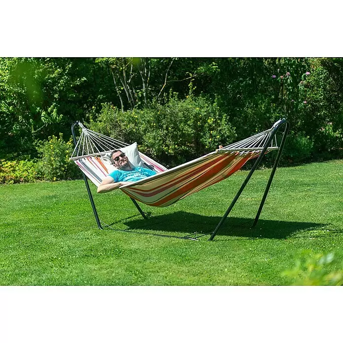 Chillounge Stabhängematte - L x B: 300 x 140 cm, Sunrise - Gestreifte Stoffhängematte mit schwarzem Metallgestell, ein Mann entspannt sich darin bequem im Freien.