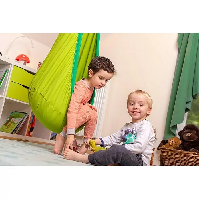La Siesta Hängesessel Joki für Kinder - Froggy - Ein Kind sitzt in einer leuchtend grünen Stoff-Sensorikschaukel und spielt mit einem anderen Kind im Zimmer mit Dinosaurier-Spielzeug.