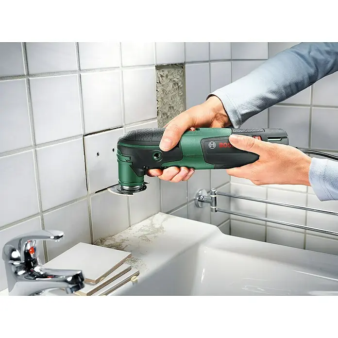 Bosch Elektro-Multifunktionswerkzeug PMF 220 CE - 220 W, STARLOCK-System - Eine Nahaufnahme eines Bosch-Multifunktionswerkzeugs beim Schneiden von Fugen zwischen weißen Fliesen im Badezimmer.