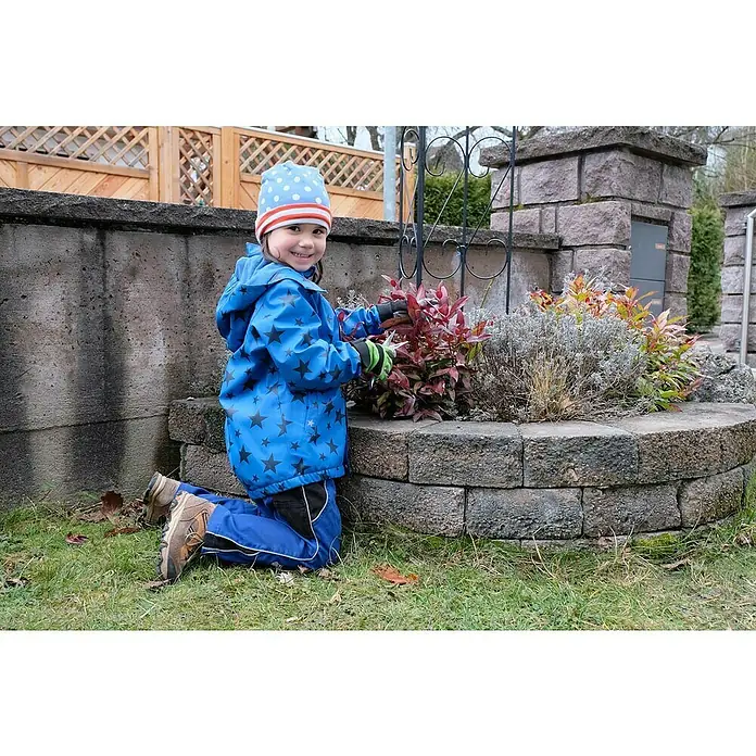 Freund Victoria Guantes de trabajo infantiles - Talla del guante: 6, Verde - Una niña con chaqueta y gorro azul está arrodillada en el jardín recortando hojas rojas con unas tijeras de podar.