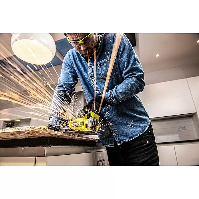 Ryobi ONE+HP Akku-Winkelschleifer RCT18C-0 - 18 V, Ohne Akku - Mann mit Schutzbrille schneidet Holz mit gelbem Ryobi Winkelschleifer, Funken sprühen.