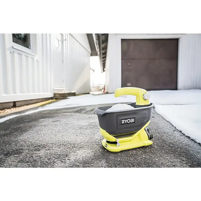 Ryobi ONE+ Handstreuer OSS1800 - 18 V, Anzahl Akkus: Ohne Akku - Ein gelb-schwarzer Ryobi-Streuwagen steht auf einer asphaltierten Fläche mit Schnee. Ideal zum Ausbringen von Salz oder Dünger im Garten.