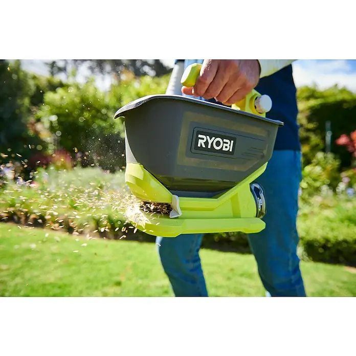 Ryobi ONE+ Handstreuer OSS180018 V, Anzahl Akkus: Ohne Akku - Nahaufnahme eines Ryobi-Streuwagens in Aktion, der Samen über einen grünen Rasen verteilt.