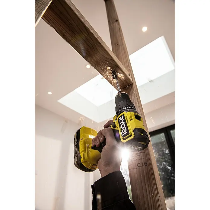 Ryobi ONE+HP Akku-Bohrschrauber RDD18C-0 - 18 V, Ohne Akku, 54 Nm - Nahaufnahme eines gelben Ryobi-Akkuschraubers beim Bohren eines Lochs in ein Holzstück mit herumfliegenden Holzspänen.