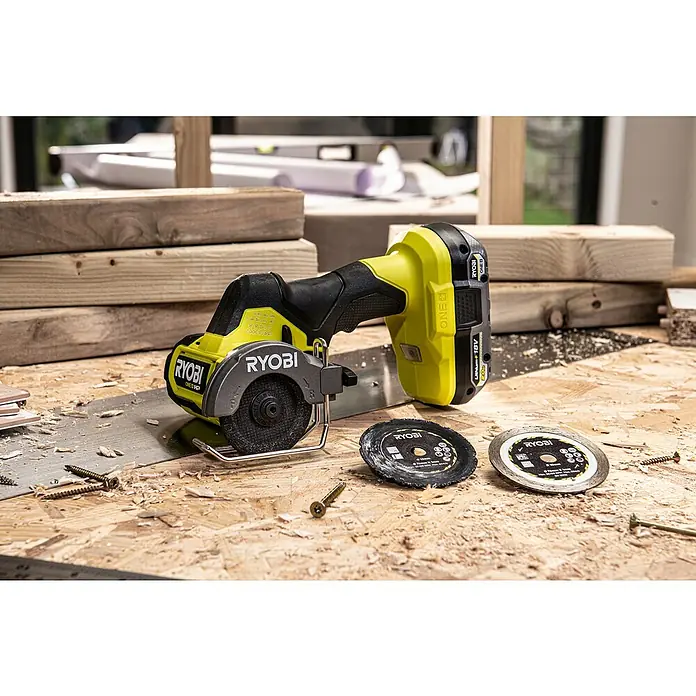 Ryobi ONE+HP Amoladora angular de batería RCT18C-0 - 18 V, Sin batería - Primer plano de una mini sierra circular inalámbrica Ryobi ONE+ con hojas de repuesto y tornillos en un banco de trabajo, ideal para cortes precisos.