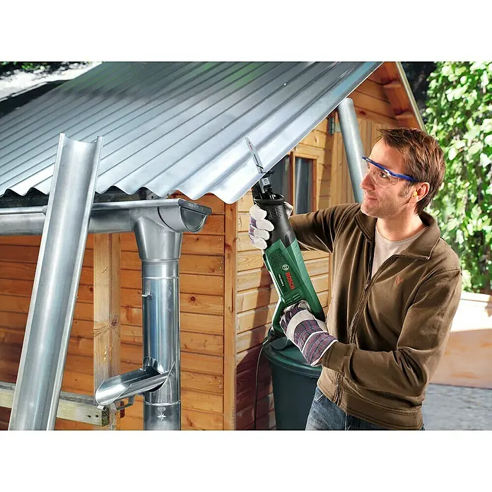 Bosch Säbelsäge PSA 900 E - 900 W, Hublänge: 28 mm, 2 Sägeblätter - Ein Mann benutzt eine Bosch Säbelsäge, um ein Blechdach zu schneiden. Die grüne Säge ist gut sichtbar und im Fokus des Bildes.