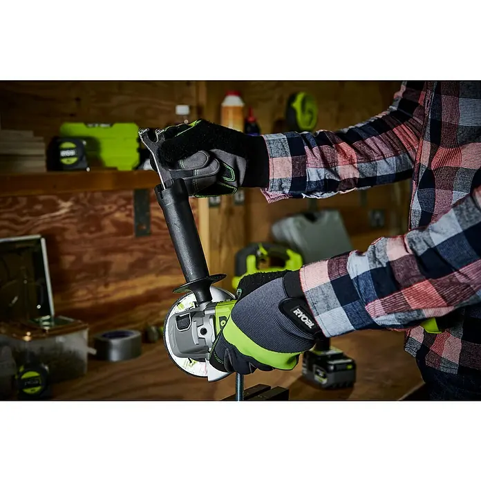 Ryobi ONE+ Akku-Winkelschleifer RAG18125-0 - Ohne Akku, Durchmesser Scheibe: 125 mm - Der Ryobi Winkelschleifer wird in einer Werkstatt mit Schutzhandschuhen bedient, um Präzision und Sicherheit bei der Arbeit zu gewährleisten.