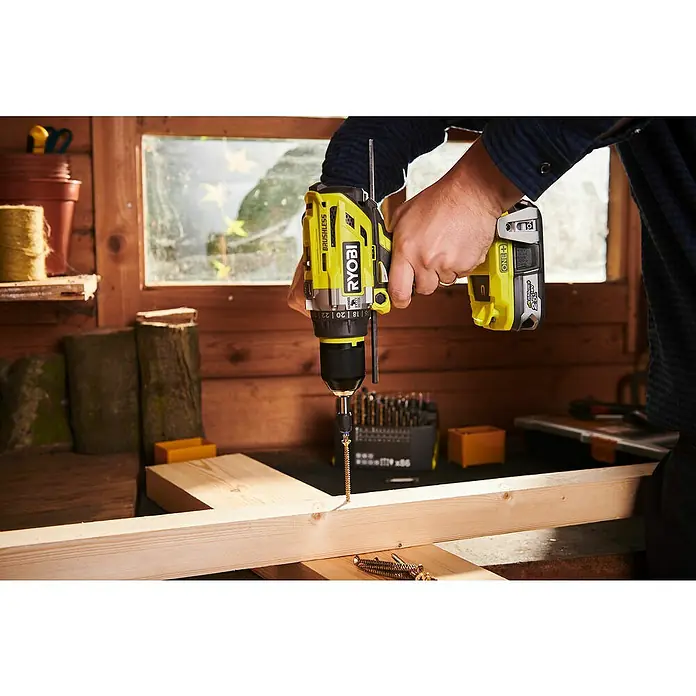 Ryobi ONE+ Akku-Schlagbohrschrauber R18PD7-252S - 18 V, 2 Akkus, 5 Ah, 85 Nm - Nahaufnahme eines Ryobi Akku-Bohrschraubers, der in ein Holzbrett geschraubt wird. Präzision und Leistung vereint für Handwerksprojekte.