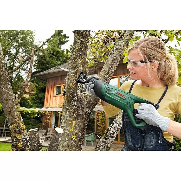 Bosch Säbelsäge PSA 900 E - 900 W, Hublänge: 28 mm, 2 Sägeblätter - Eine Frau mit Schutzbrille und Handschuhen benutzt eine grüne Bosch PSA 9000 E Säbelsäge zum Baumschnitt im Freien.
