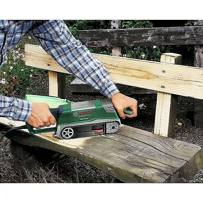 Bosch Lijadora de banda eléctrica de sobremesa PBS 75 AE - 750 W - Persona lijando una tabla de madera al aire libre con una lijadora de banda verde Bosch PBS 75 AE.