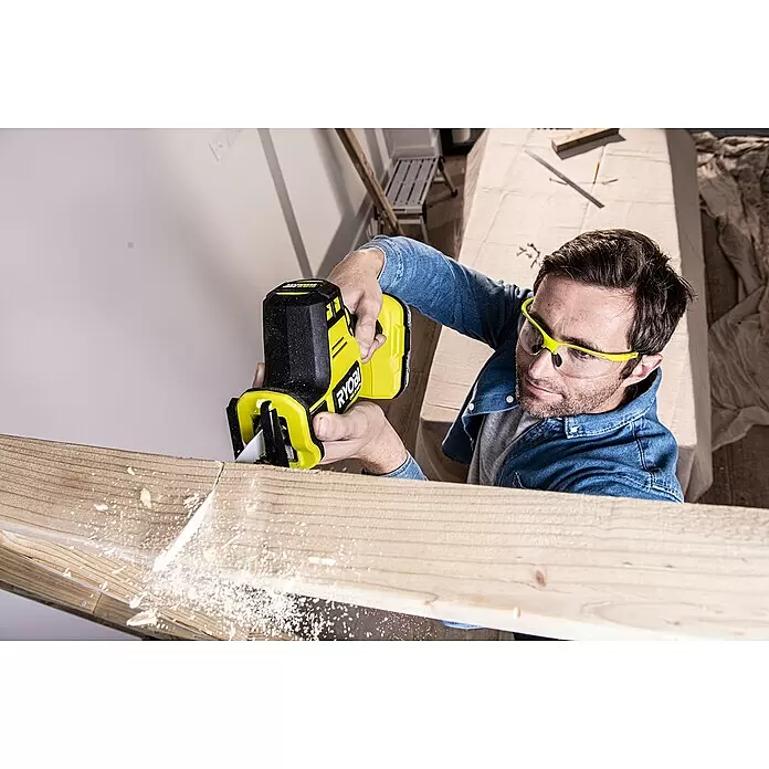 Ryobi ONE+HP Akku-Säbelsäge RRS18C-0 - 18 V, Li-Ionen, Ohne Akku, 3.300 U/min - Mann mit Schutzbrille benutzt eine gelb-schwarze Ryobi Säbelsäge, um einen Holzbalken zu sägen, dabei entsteht Sägemehl.