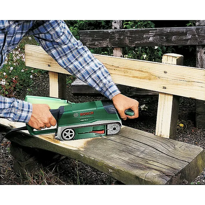 Bosch Elektro-Bandschleifmaschine PBS 75 A - 710 W, Bandgeschwindigkeit: 300 m/min - Handwerker schleift Holzbank mit grünem Bosch Bandschleifer. Der Bosch Schleifer glättet die Oberfläche der alten Bank im Garten.