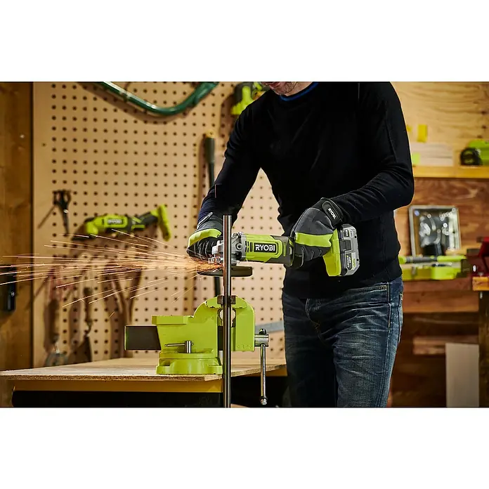 Ryobi ONE+ Akku-Winkelschleifer RAG18125-0 - Ohne Akku, Durchmesser Scheibe: 125 mm - Ein Arbeiter benutzt einen Ryobi-Winkelschleifer, um an einer Werkbank Metall zu bearbeiten, wobei Funken sprühen. Schutzkleidung ist vorhanden.